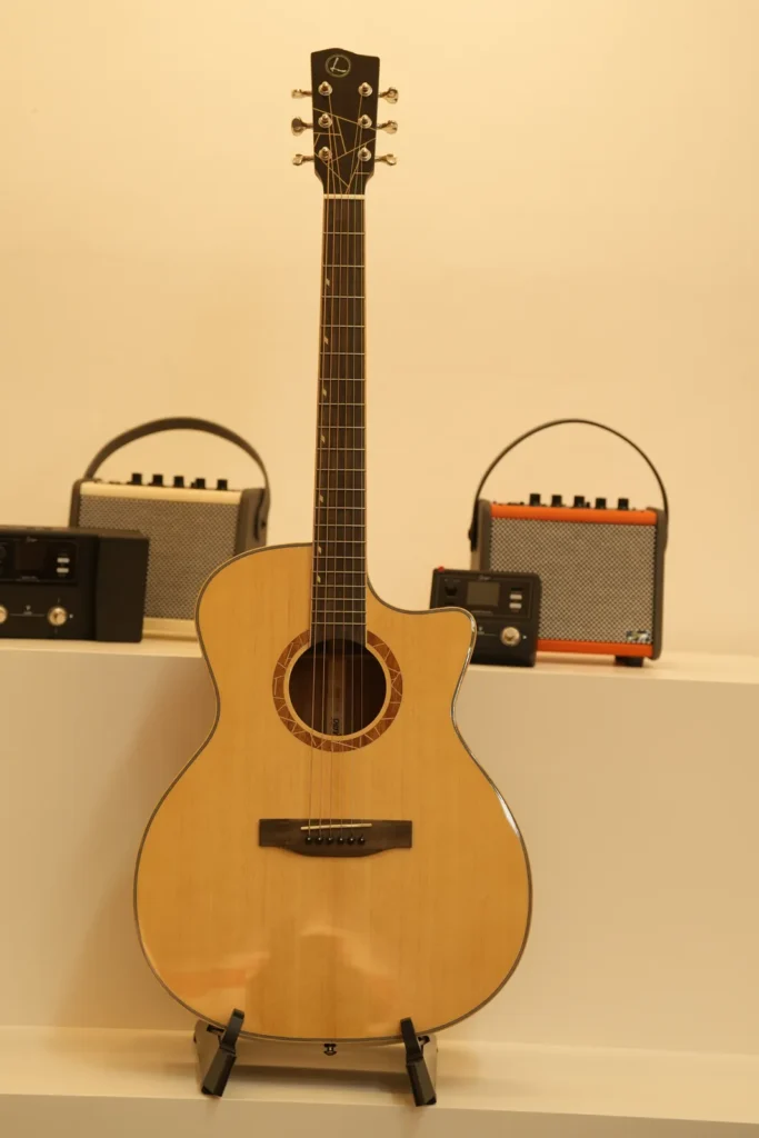 Fotografía real de una guitarra acústica en un soporte, con amplificadores al fondo